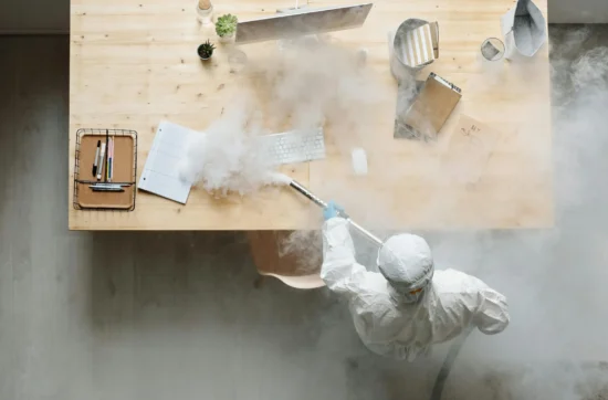 A Person in a Protective Suit Fumigating a Table